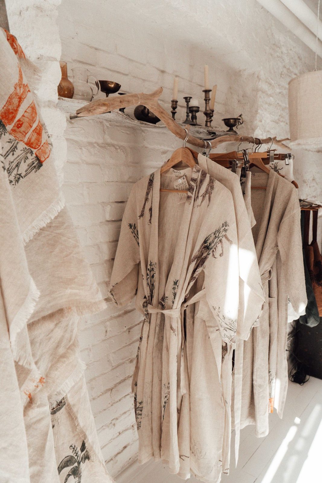 Beyaz badanalı bir butik duvarında güneş ışığı altında asılı krem tonlu elbiseler